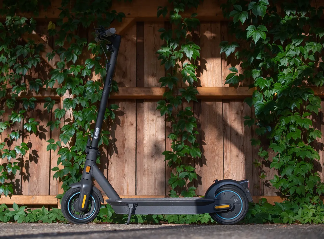 Trottinette électrique posée contre une palissade en bois couverte de lierre