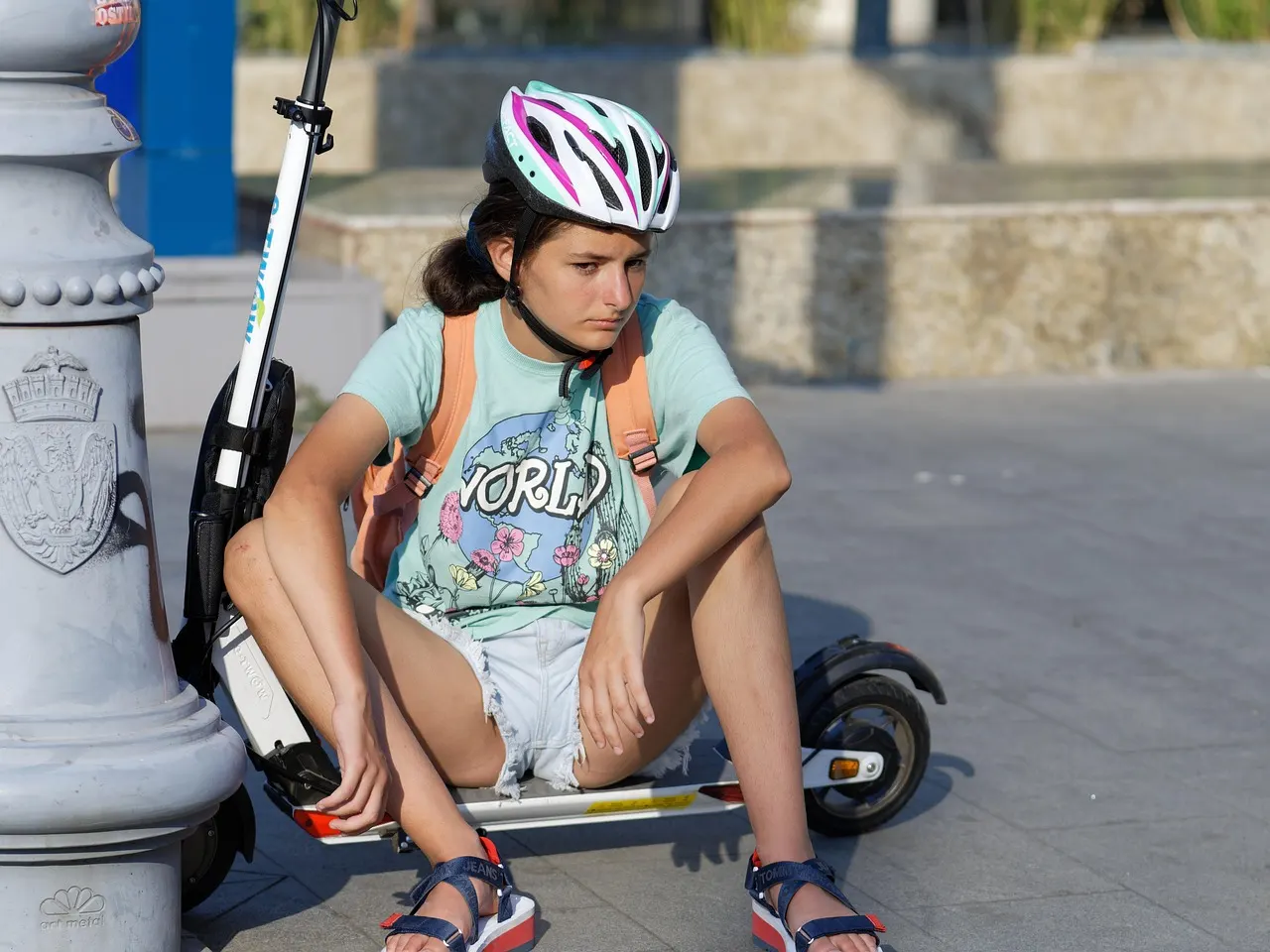 Adolescente casquée assise à côté de sa trottinette électrique