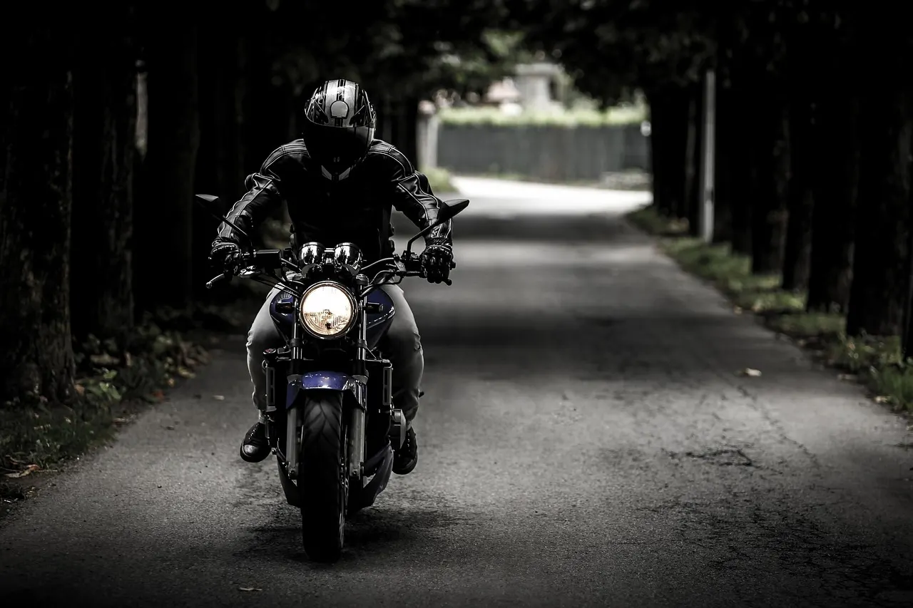 Motard casqué sur une route bordée d’arbres, phare allumé