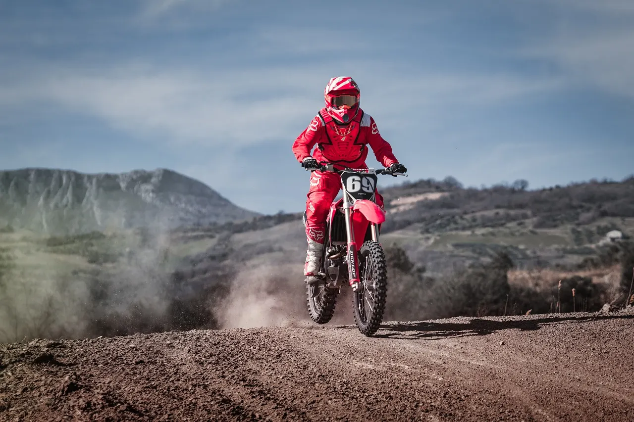 Pilote de motocross en tenue rouge sur un terrain de terre